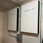 A home battery storage unit mounted on a wall beside rooftop solar equipment